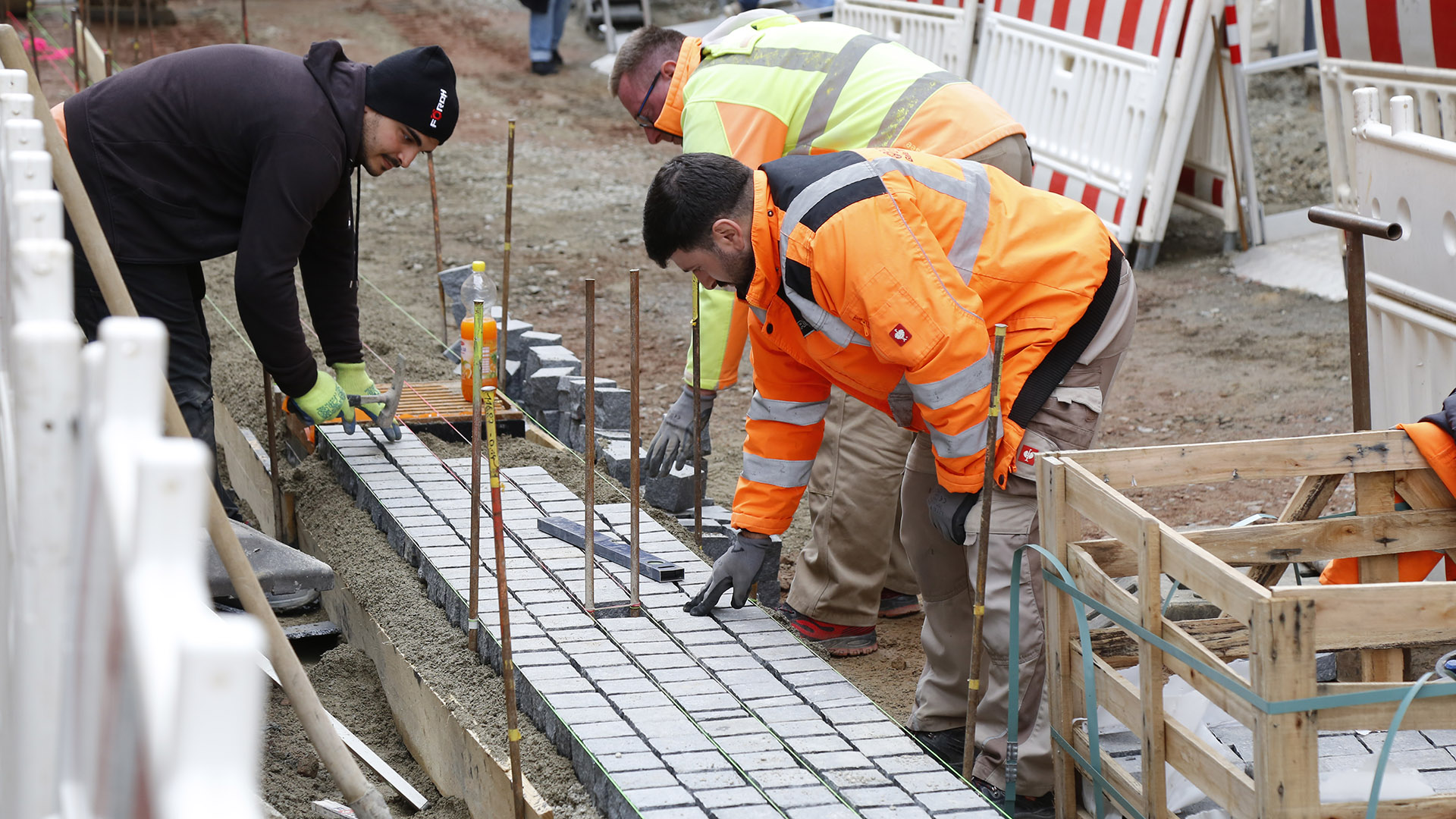 Drei Bauarbeiter verlegen neue Pflastersteine in der Fugngerzone.